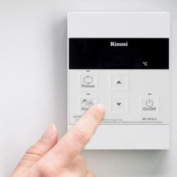 A close-up of a white Rinnai wall-mounted thermostat control panel being pressed by a person's finger. The panel has a black top section with the Rinnai logo and temperature icon, and white buttons for Preheat, directional arrows, and On/Off.